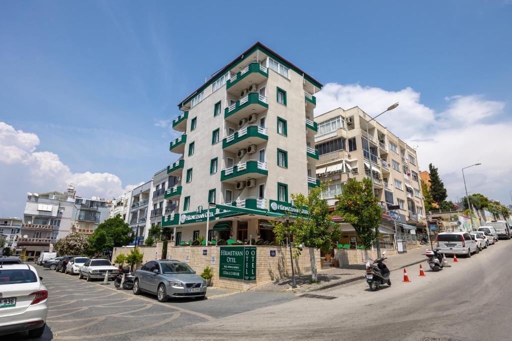 a tall white building with cars parked in a parking lot at Hikmethan Otel in Kusadası