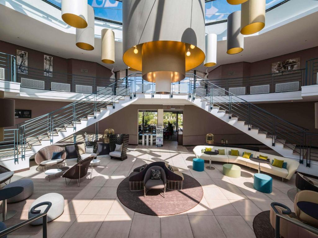 a lobby of a building with a staircase and chairs at Novotel La Grande Motte Golf in La Grande Motte