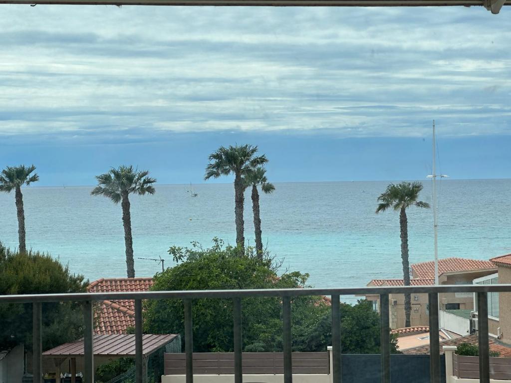 d'un balcon avec des palmiers offrant une vue sur l'océan. dans l'établissement Appartement vue mer , plage à 50m, à Six-Fours-les-Plages