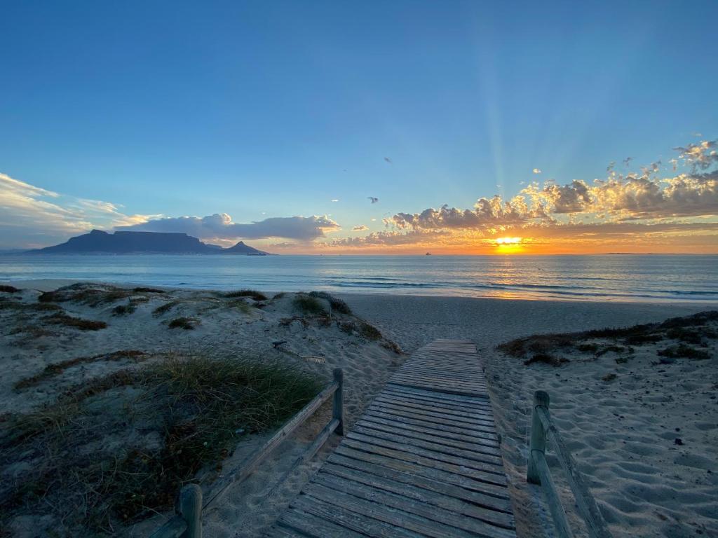 a wooden pathway to the beach with the sunset in the background at Peach on Beach Boutique Guesthouse in Bloubergstrand