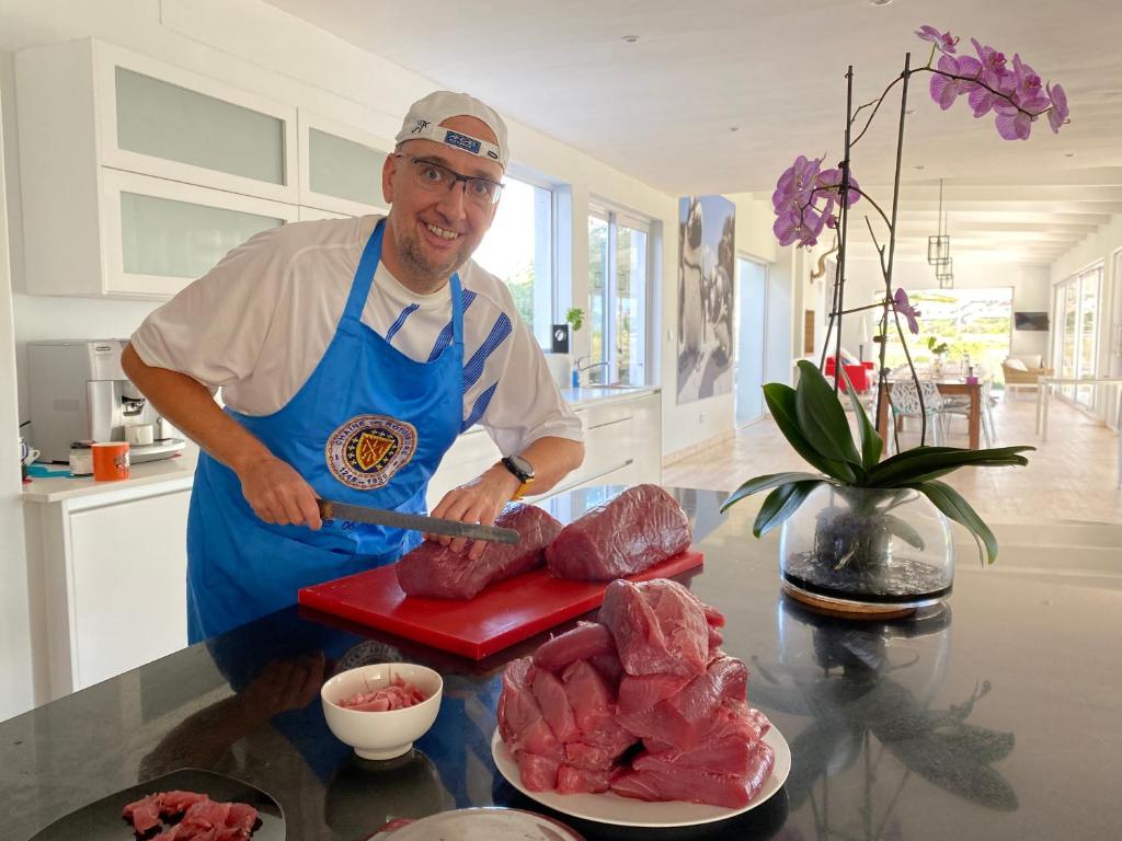 a man in a kitchen preparing meat on a cutting board at Peach on Beach Boutique Guesthouse in Bloubergstrand