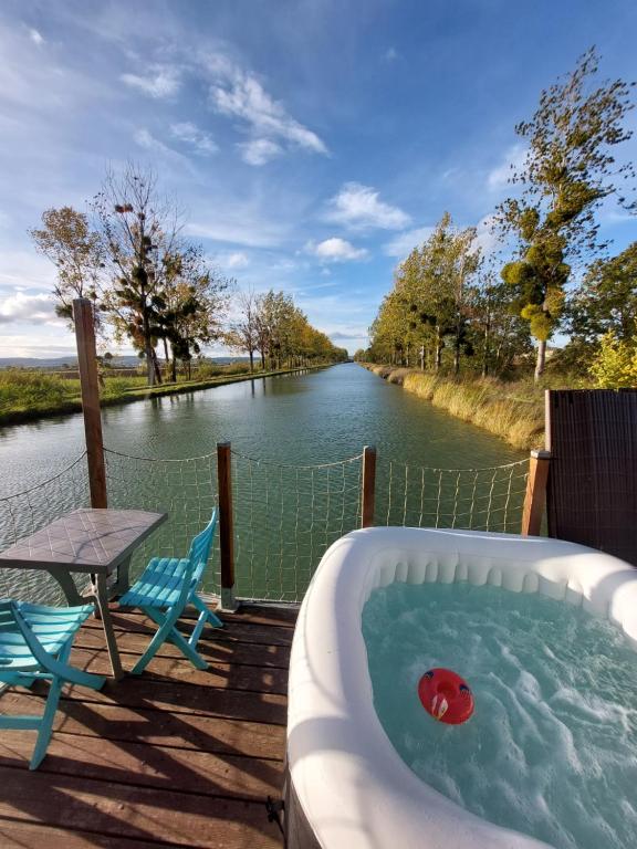 eine Badewanne auf einem Deck neben einem Fluss in der Unterkunft Cottage flottant terrasse jacuzzi option aux Portes de Dijon 