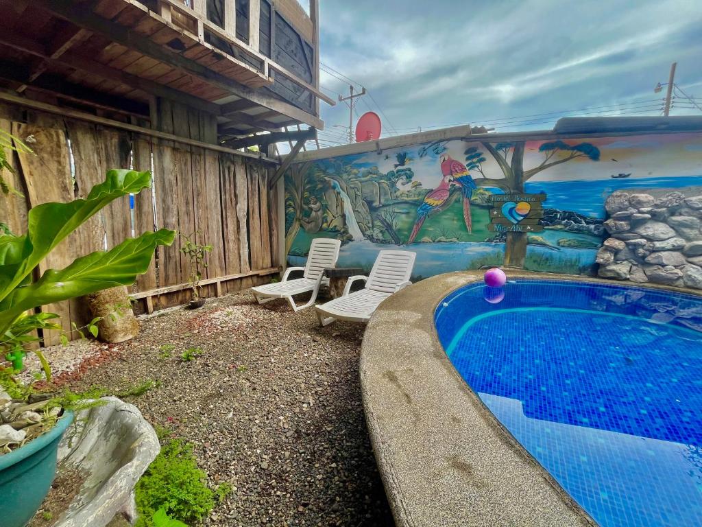 a swimming pool with two chairs and a mural at Hostel Rústico MarAbi in Tarcoles