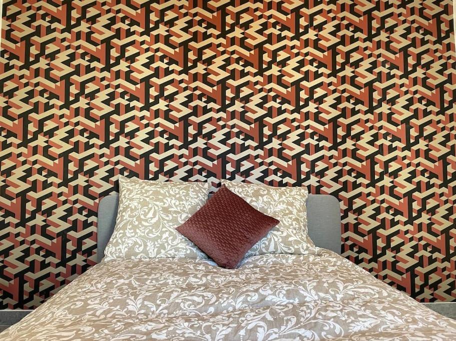 Bett mit einem Kissen vor einer gemusterten Wand in der Unterkunft Apartment Secret room Paris-Stade de France in Aubervilliers