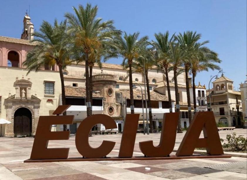 a large sign in front of a building with palm trees at Apartamentos Almenas in Écija