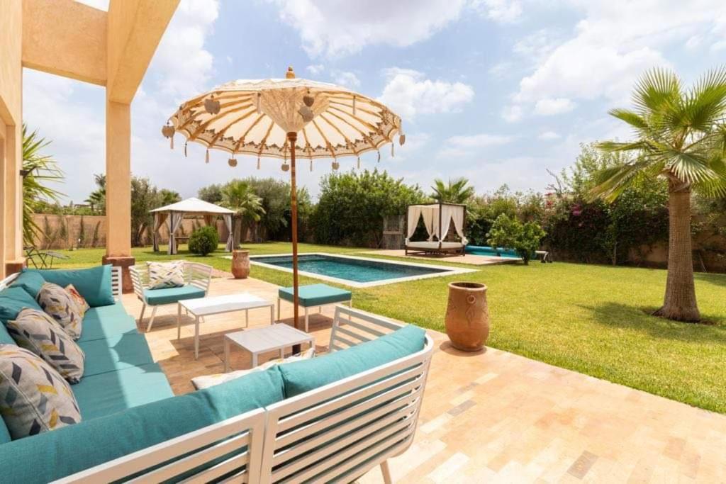 un patio con sofá, sombrilla y piscina en VILLA EDEN Marrakech RESIDENCE APPLE GARDEN 2000m2, en Marrakech