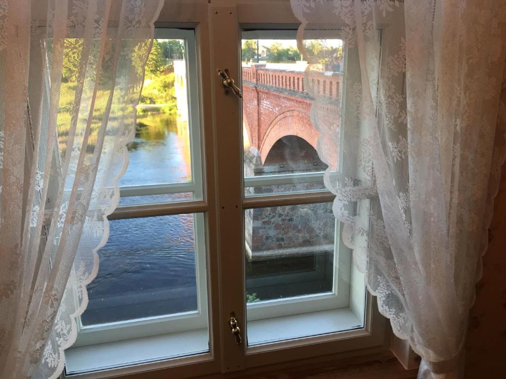 a window with white curtains and a view of a bridge at Apartamenti Kuldīgas Pilsdzirnavas in Kuldīga