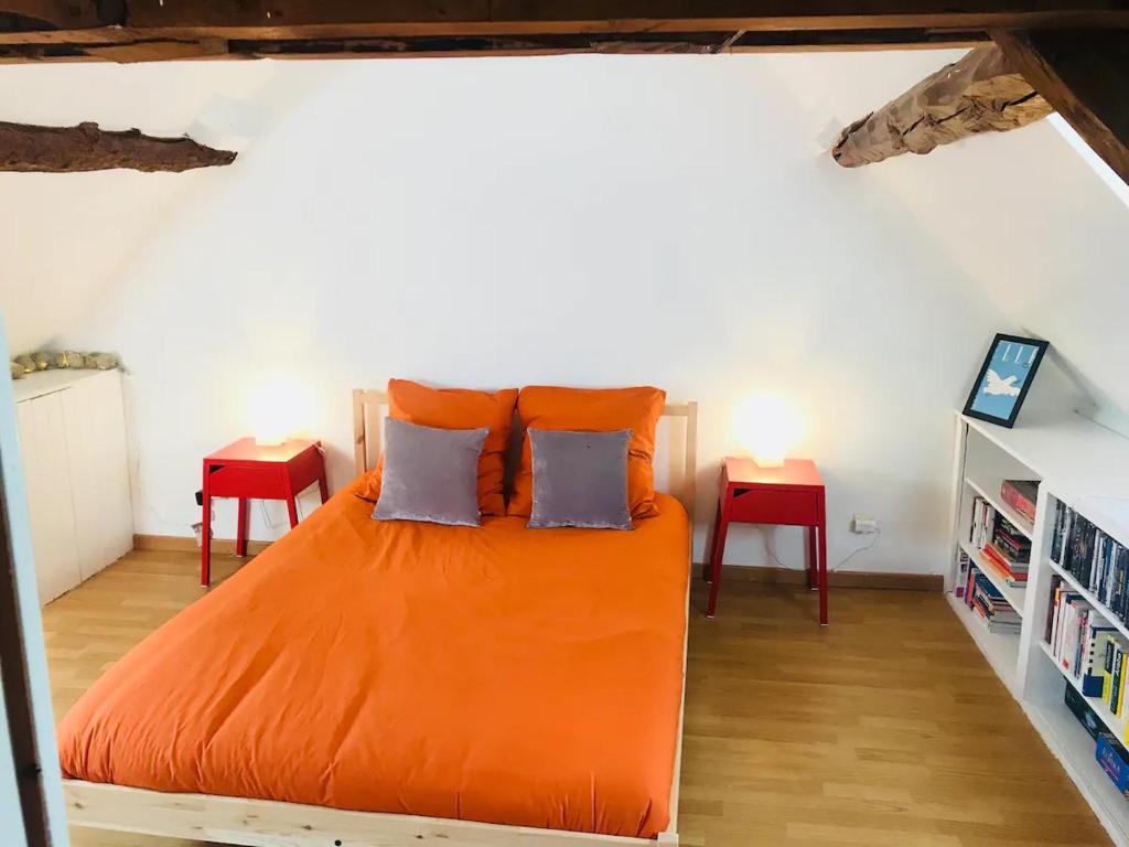 1 cama naranja en una habitación con 2 mesas en Jolie Maison dans le Perche, en Mahéru
