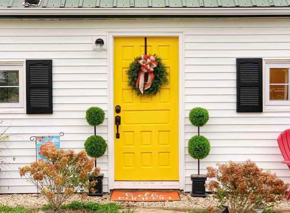 eine gelbe Tür auf einem weißen Haus mit Kranz in der Unterkunft Green Acres Farmhouse Fugitive Beach/Military/MS&T in Rolla