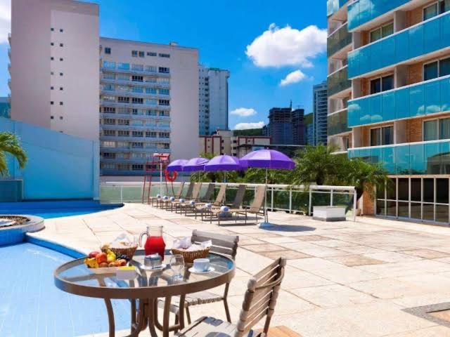 patio ze stołem, krzesłami i fioletowymi parasolami w obiekcie Flat em hotel Mercure w mieście Nova Iguaçu