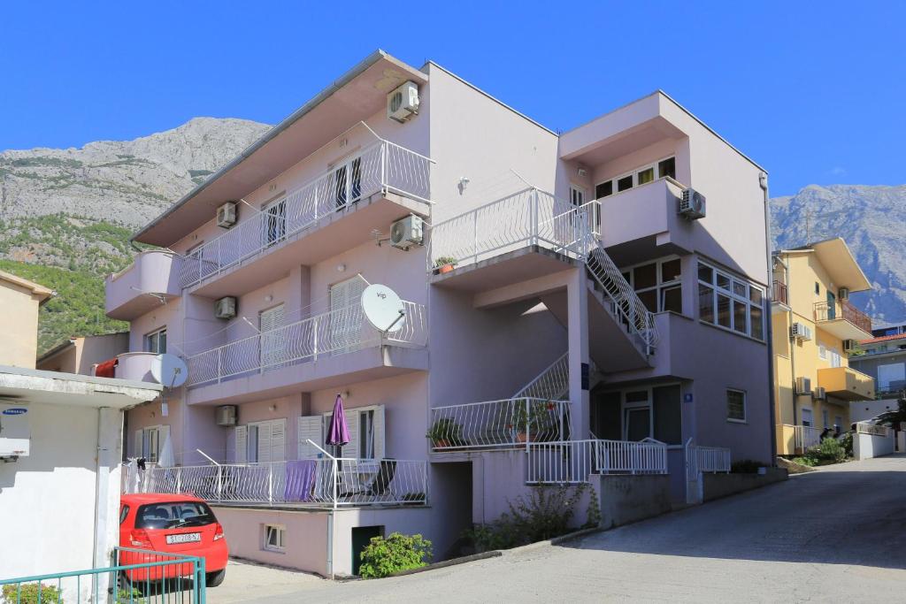 a pink apartment building with a red car parked in front at Apartments by the sea Baska Voda, Makarska - 21774 in Baška Voda