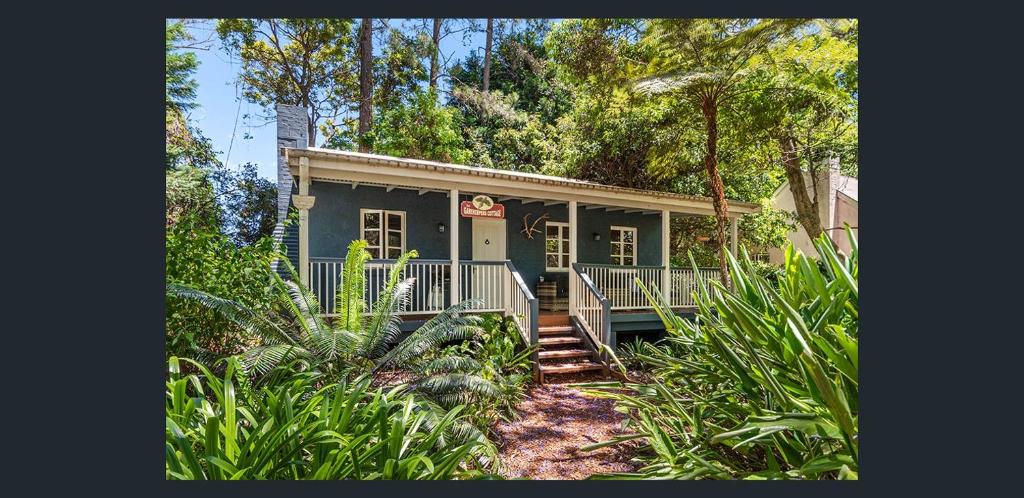 a small blue house with a porch and trees at The Gamekeepers Spa Cottage in Tamborine Mountain in Mount Tamborine