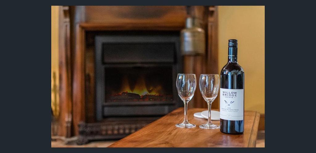 a bottle of wine and two glasses on a table with a fireplace at The Gamekeepers Spa Cottage in Tamborine Mountain in Mount Tamborine