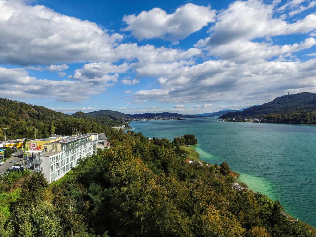 a view of a river with a building on a hill at ibis Wörthersee in Pörtschach am Wörthersee