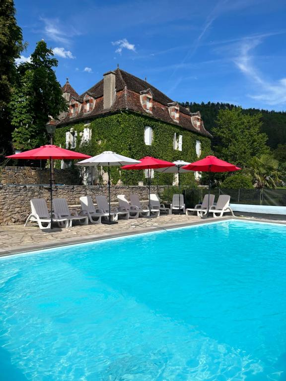 a pool with chairs and umbrellas in front of a building at Maison Redon chambres d'hôtes in Tour-de-Faure