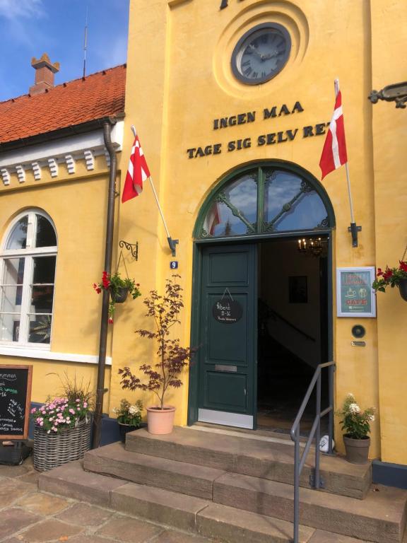 un edificio amarillo con una puerta verde y dos banderas en Cafebrumman, en Neksø