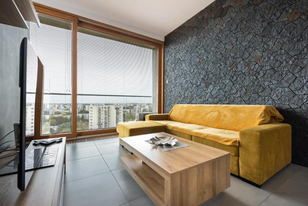 a living room with a yellow couch and a table at Metro Imielin 13th Floor Apartment by BookingHost in Warsaw