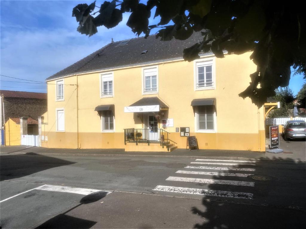 ein gelbes Gebäude mit schwarzem Dach auf einer Straße in der Unterkunft Le 120 - Groupe Logis Hotels - Ex Auberge la Terrasse in La Châtaigneraie