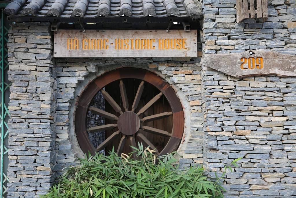 a building with a wooden wheel in a stone house at Ha Giang Historic House & tour in Ha Giang