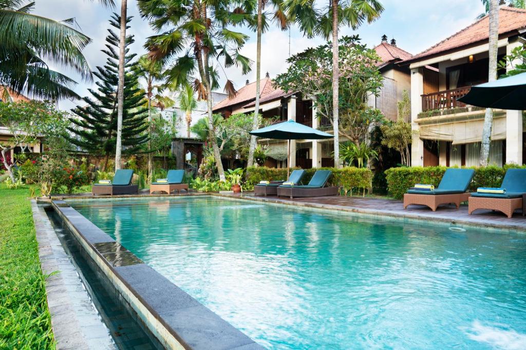 een zwembad in een resort met blauwe stoelen en palmbomen bij Ubud Tropical Garden in Ubud