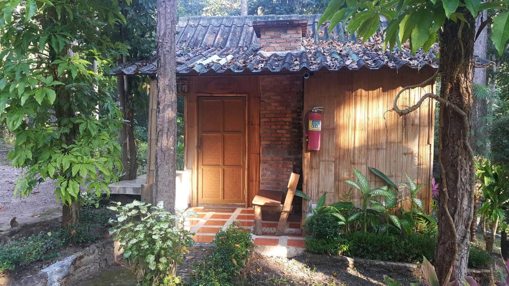 Una pequeña casa con una puerta de madera en un jardín en ลิ้นฟ้าแคมป์ปิ้งรีสอร์ท, en Mae Hong Son