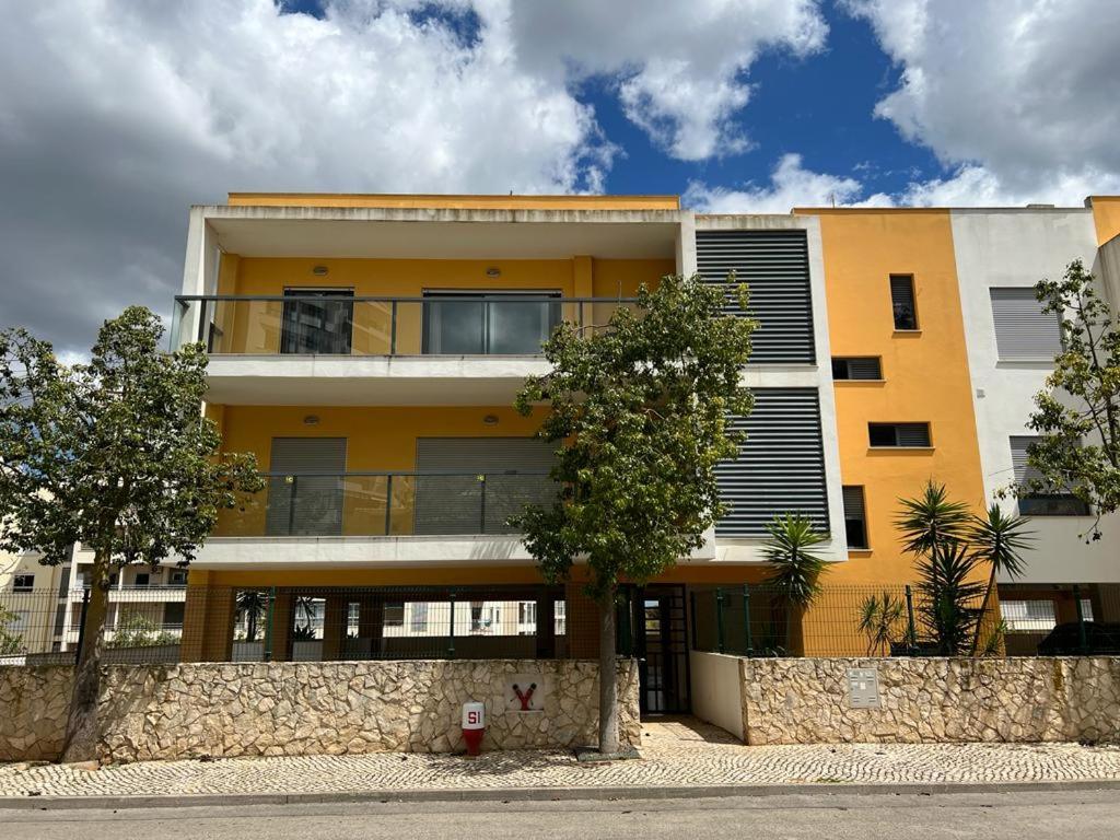un edificio amarillo con un árbol delante de él en Apartamento Vila Rosa - PRAIA DA ROCHA, en Portimão