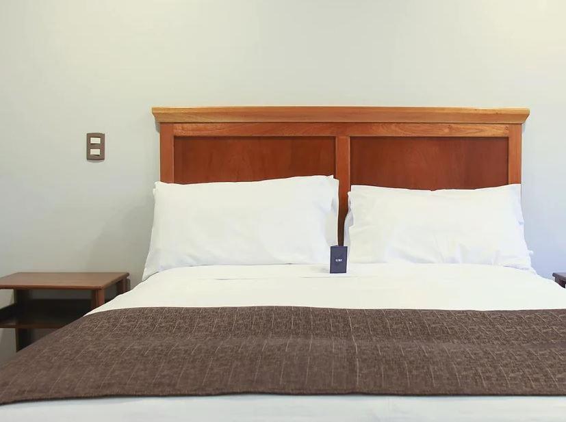 1 cama con cabecero de madera y almohadas blancas en ManglesChicama, en Lima