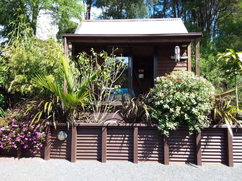 a small wooden cabin with flowers and plants at The Bali Room in Coromandel Town
