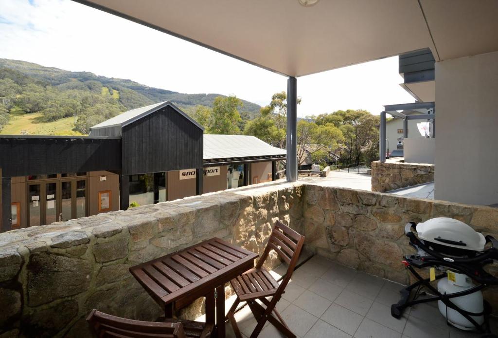 a balcony with two chairs and a grill on a stone wall at Squatters Run 1 in Thredbo