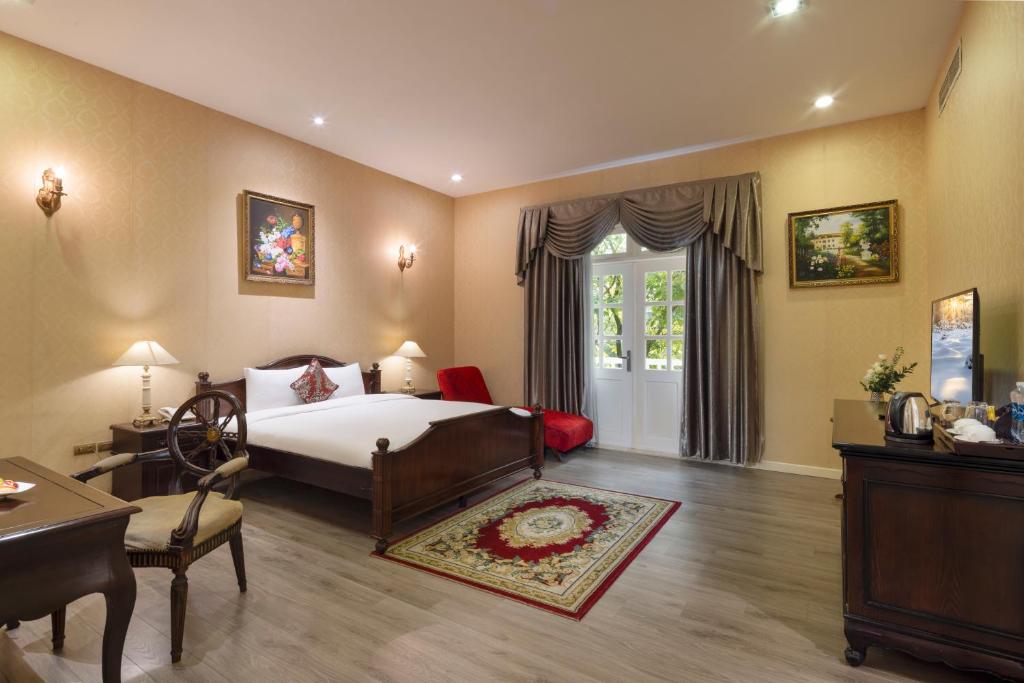 ein Schlafzimmer mit einem Bett, einem Tisch und einem Stuhl in der Unterkunft Hidden Mansions Saigon Resort in Ho-Chi-Minh-Stadt