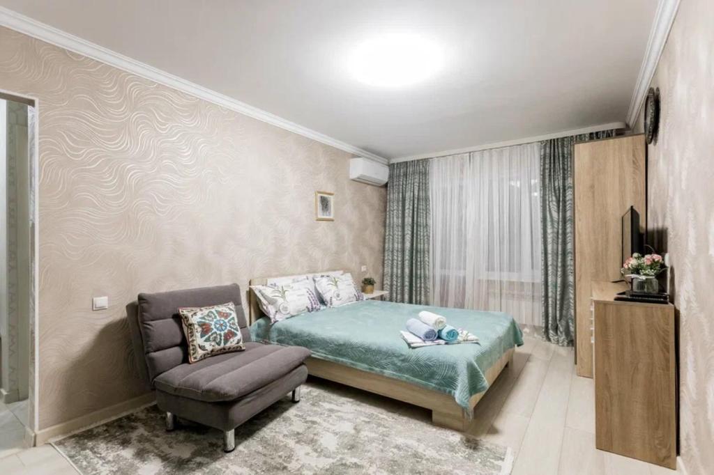 een slaapkamer met een bed en een stoel bij Уютная квартира на Арбате in Alma-Ata