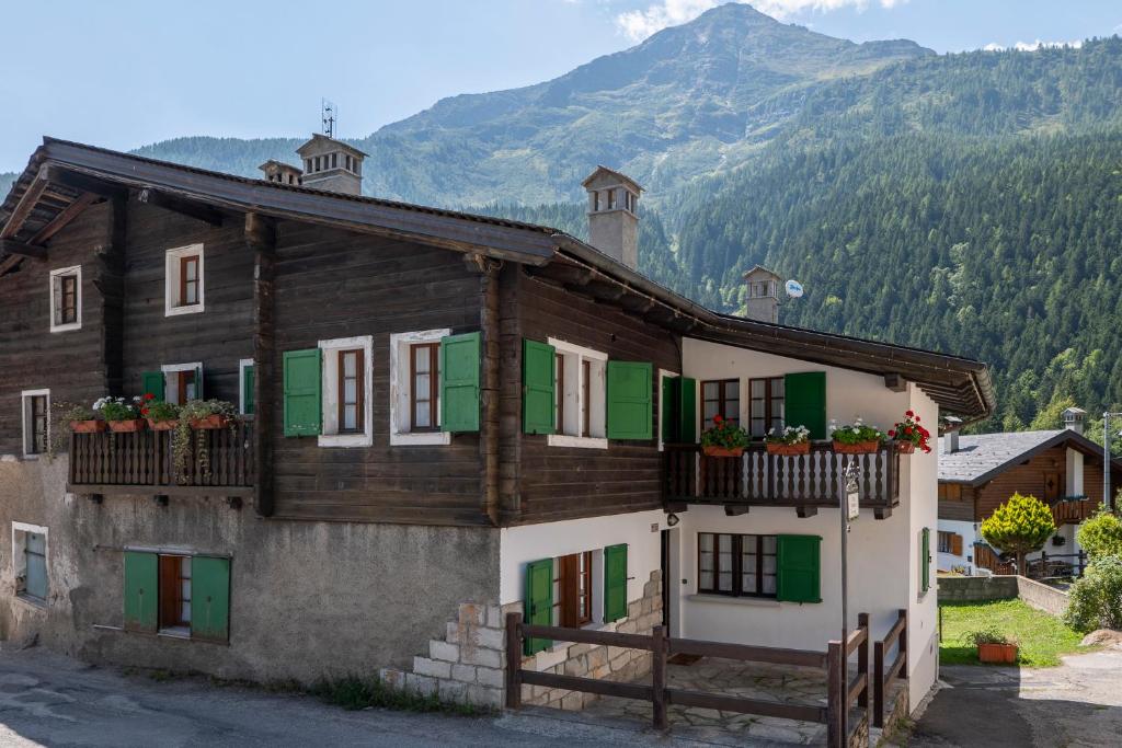 uma casa com janelas verdes e brancas e uma montanha em Incanto Walser Apartments Ronco em Macugnaga