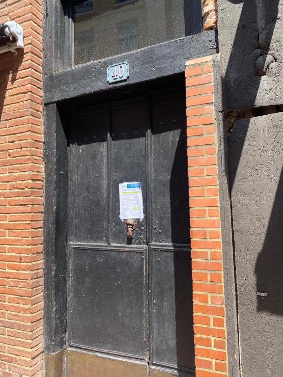 une porte noire avec un panneau dans un bâtiment en briques dans l'établissement petit appartement cosy, à Toulouse