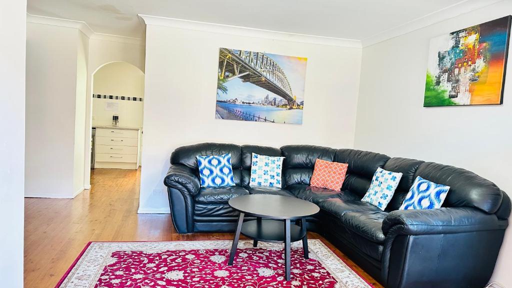 ein Wohnzimmer mit einem schwarzen Ledersofa und einem Tisch in der Unterkunft Quiet family Townhouse in Wollongong CBD in Wollongong