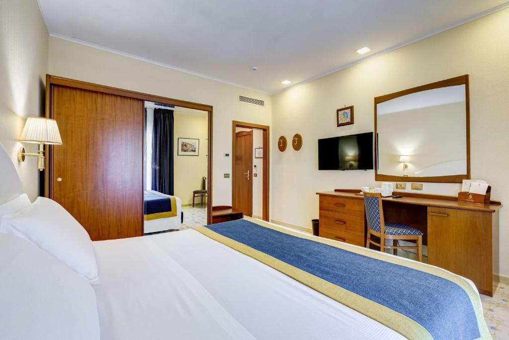 1 dormitorio con cama, escritorio y espejo en Best Western Hotel La Solara, en Sorrento