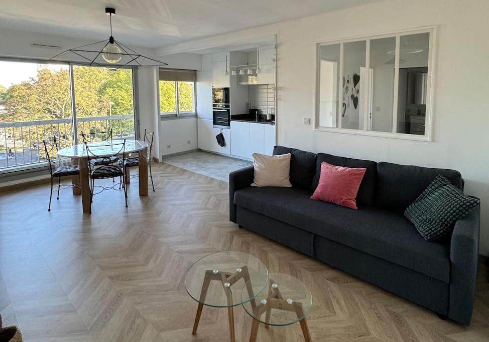 a living room with a couch and a table and a kitchen at Appartement neuf avec balcon et parking privé in Caen