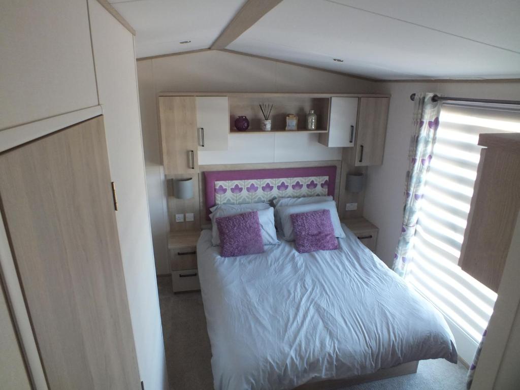 a small bedroom with a bed with purple pillows at Beachside Lighthouse 14 in Lossiemouth