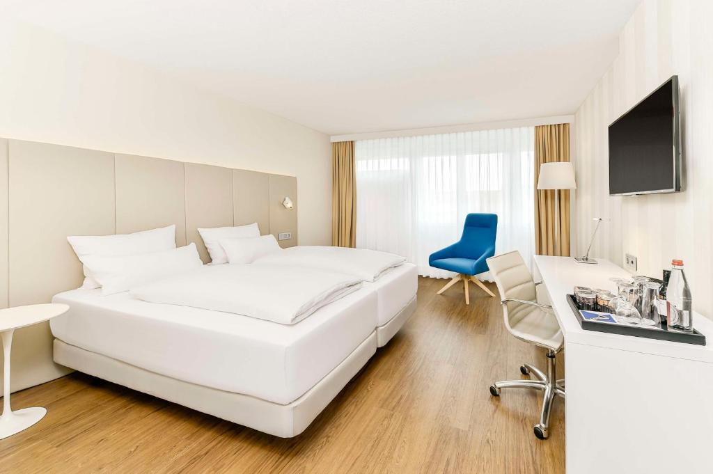 - une chambre blanche avec un grand lit blanc et une chaise bleue dans l'établissement NH Erlangen, à Erlangen