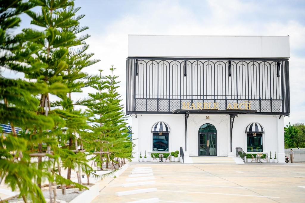 a white building with a balcony and trees at Marble Arch De Loei Hotel in Loei