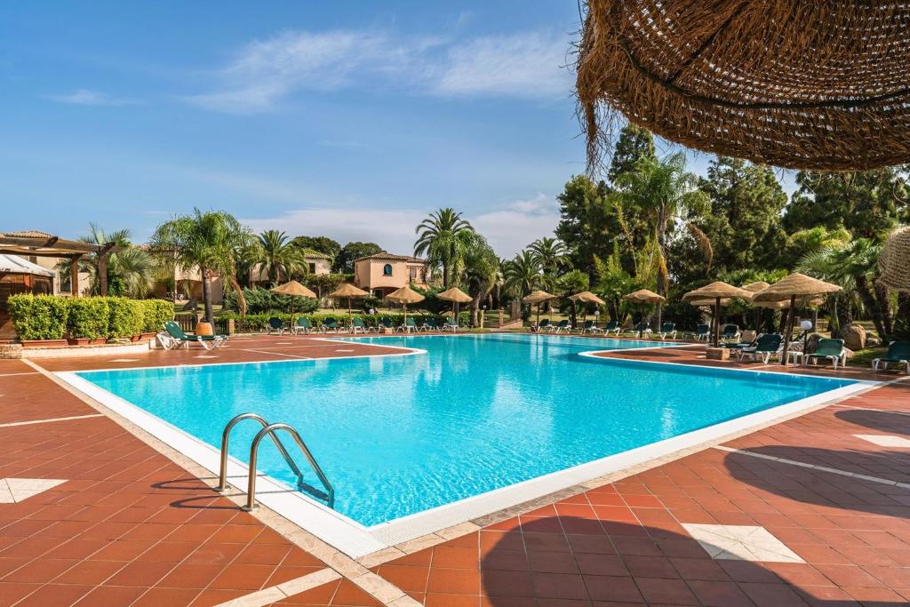 a swimming pool with chairs and umbrellas at a resort at Apartments in residence with swimming pool in Santa Margherita di Pula, 250 meters from the sea in Pula
