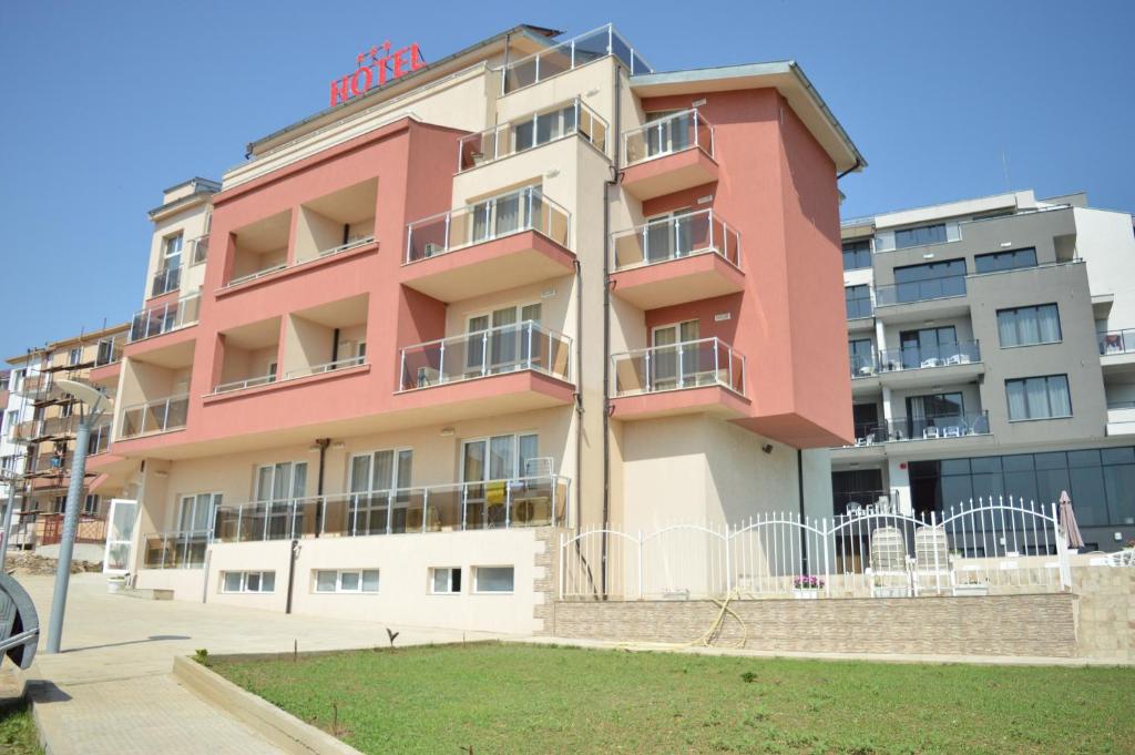 ein rosafarbenes Apartmenthaus mit Rasen davor in der Unterkunft Hotel Ray in Sozopol
