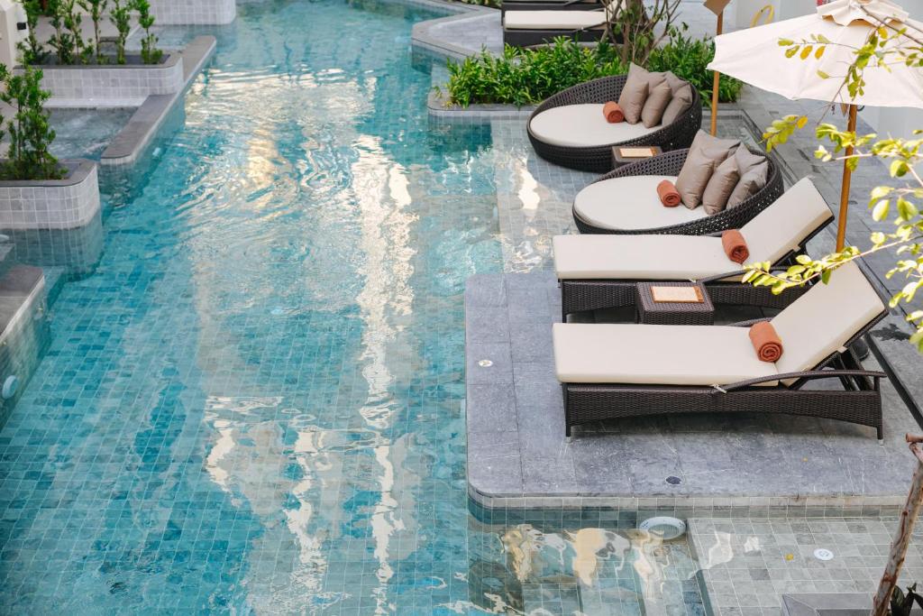 A turquoise pool bordered by cushioned loungers and round daybeds.