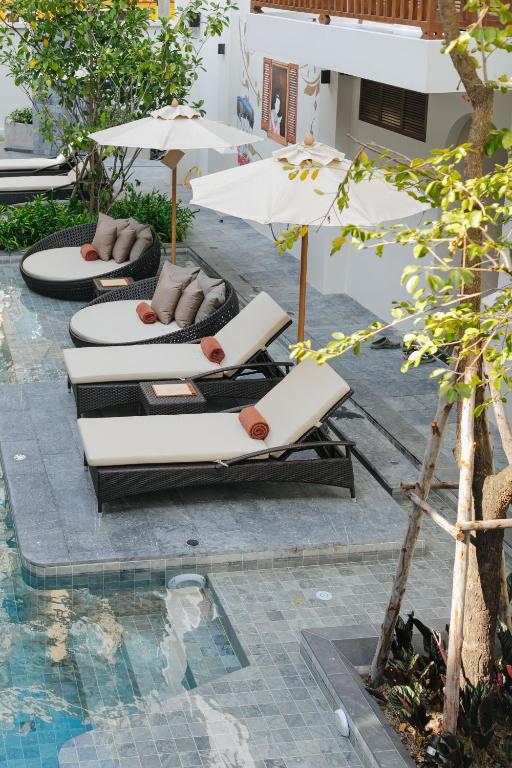 Poolside loungers and daybeds sit beneath white umbrellas beside a compact pool.