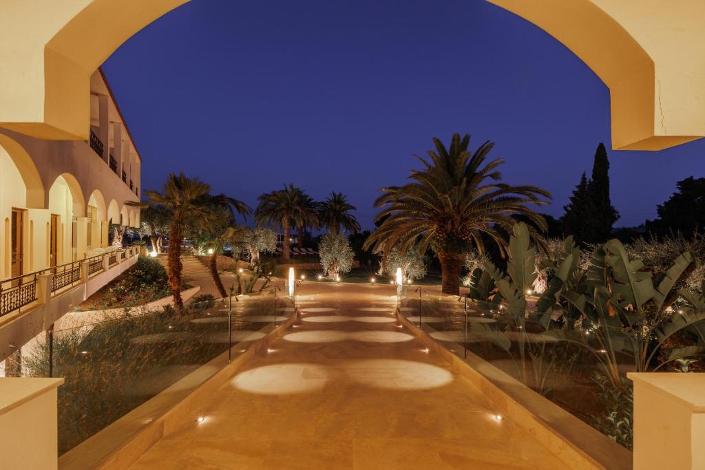 une passerelle avec des palmiers et des lumières la nuit dans l'établissement Paradise Hotel Corfu, à Gouviá