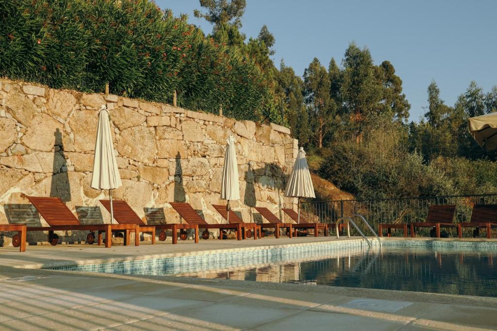 una piscina con sillas y sombrillas junto a una pared de piedra en I Love Dão Casas Da Fraga, en São Gemil