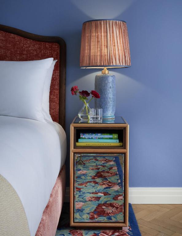 a bedside table with a lamp and a vase with flowers on it at Broadwick Soho in London