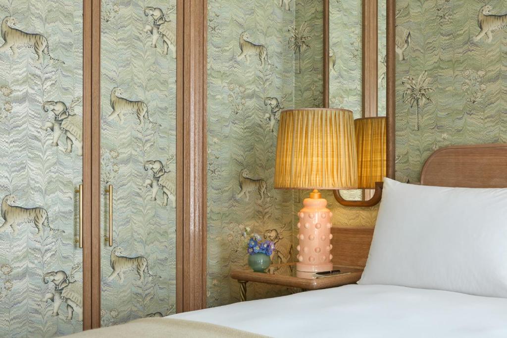 a bedroom with a bed with a lamp and wallpaper at Broadwick Soho in London