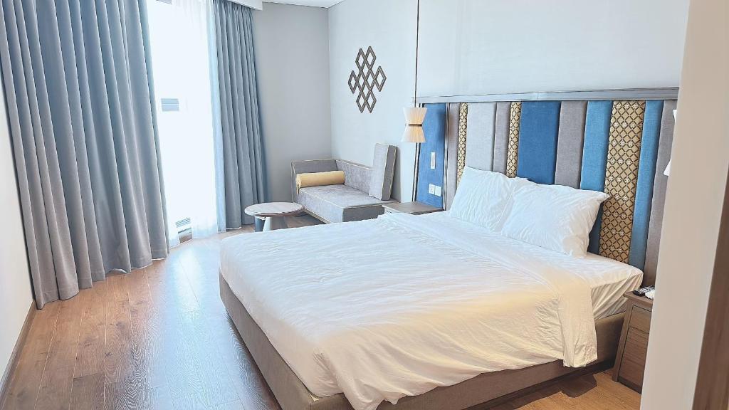 a bedroom with a large white bed and a chair at Apec Mandala Mũi Né in Ấp Long Sơn