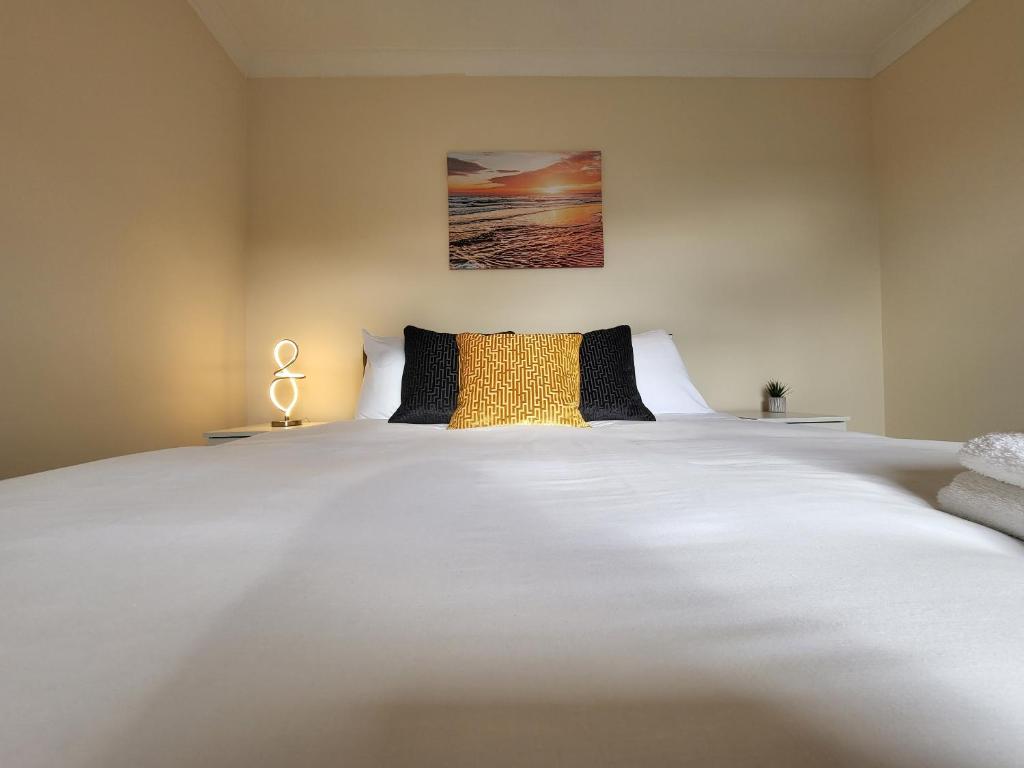 a large white bed with a yellow pillow on it at Tooting Bec Central Apartment by London Tube in London
