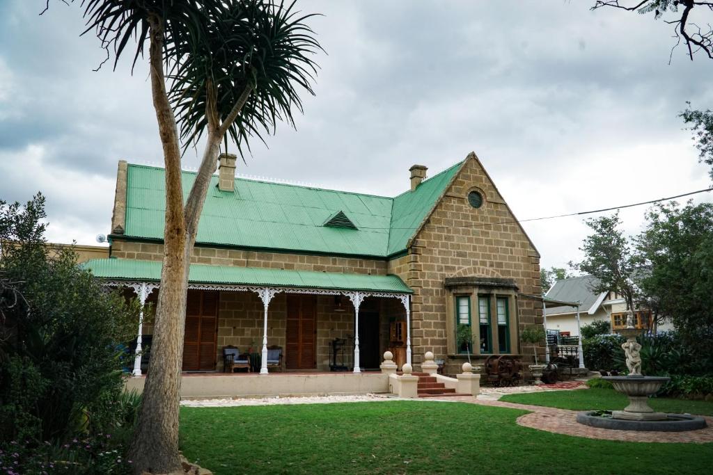 a house with a green roof and a palm tree at Outentique Accommodation in Oudtshoorn